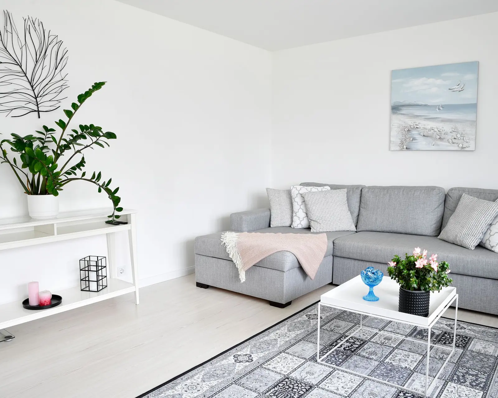 Jasny salon po home stagingu: szara sofa, rośliny i białe ściany